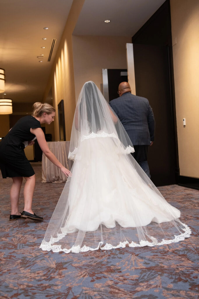 On the blog why you should hire a wedding planner - Wedding Planner Blue Sapphire Events straightens the train on a bride's dress.
