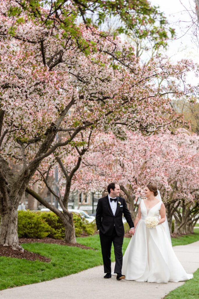 A bride and groom walk outside under the Cherry Blossoms at a Baltimore Museum of Art Wedding planned by Blue Sapphire Events.